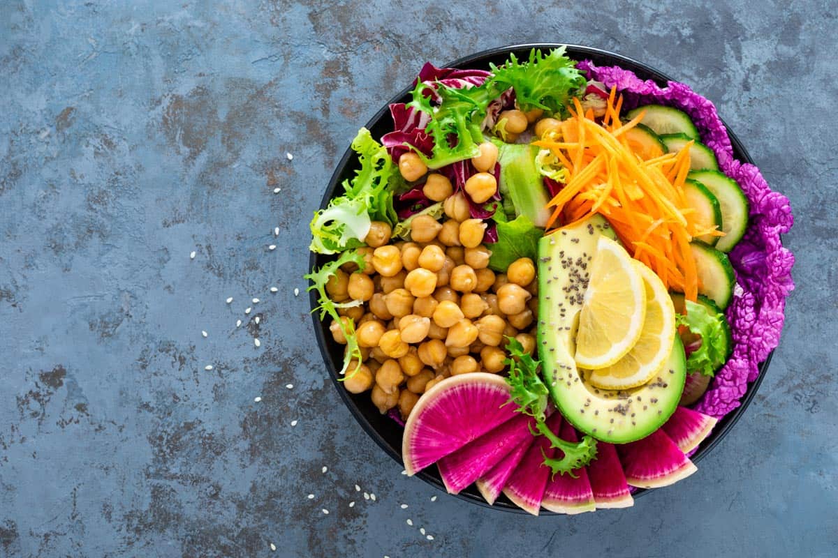 Salad Buddha bowl with fresh cucumber, avocado, watermelon radish, raw carrot, lettuce and chickpea for lunch. Healthy vegetarian food. Vegan vegetable dish. Top view