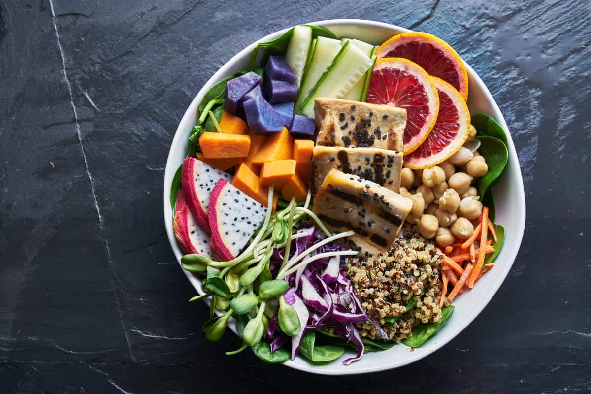 colorful buddha bowl with grilled tofu and pea shoots on dark background top view