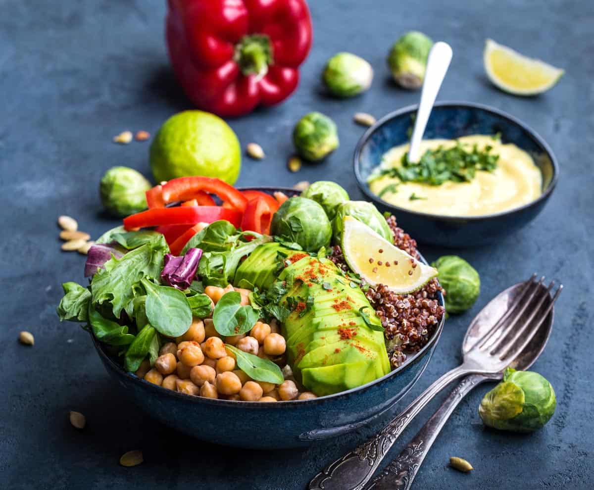 Bowl with healthy salad and dip. Close-up. Buddha bowl with chickpea, avocado, quinoa seeds, red bell pepper, fresh spinach, brussels sprout, lime mix. Vegetarian salad. Clean healthy eating concept