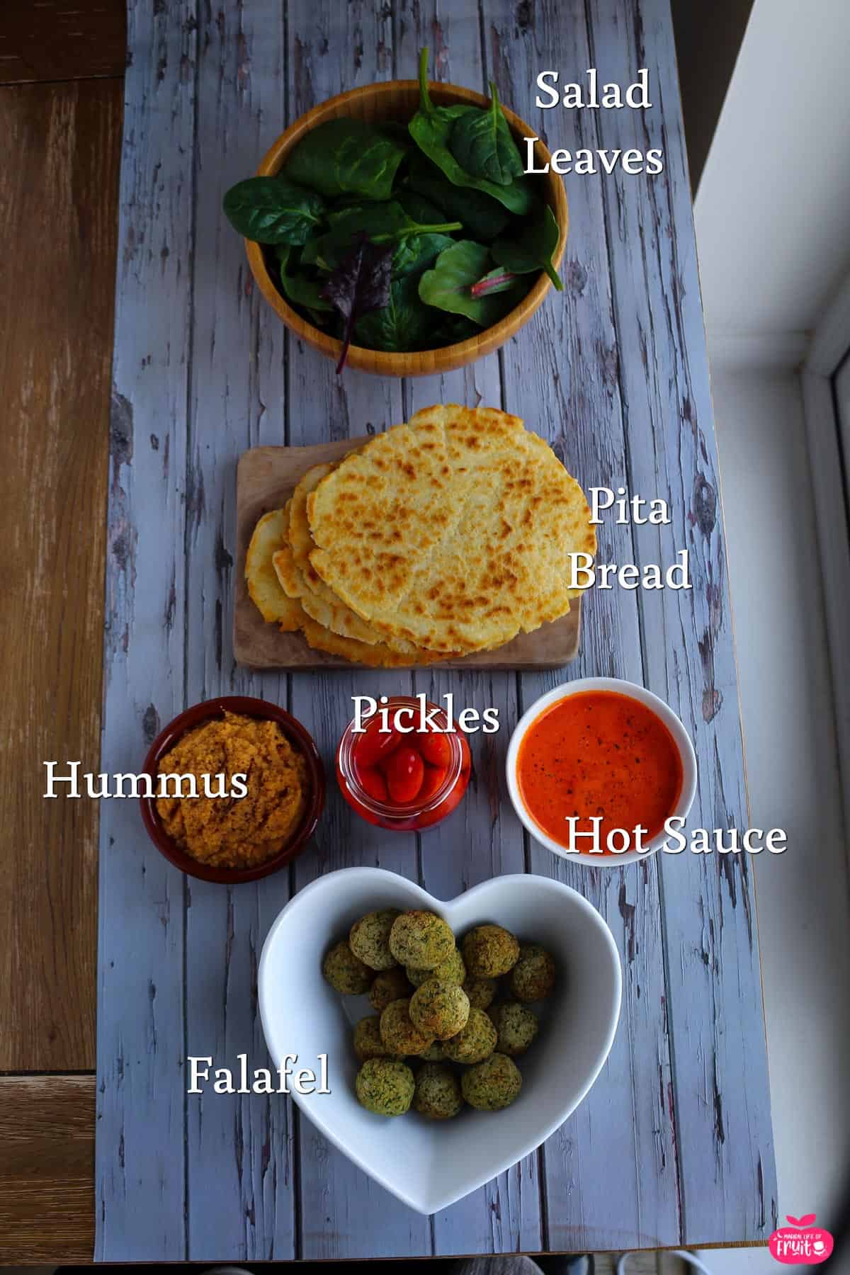 Ingredients for Falafel Gyro Recipe, salad leaves, pita bread, hummus, pickles, hot sauce and falafels.
